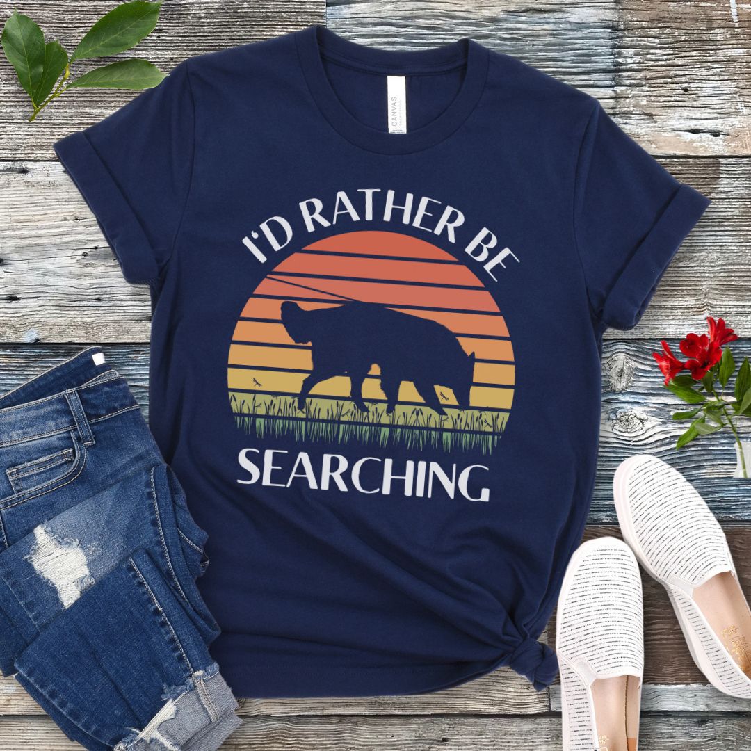 Navy blue nosework t-shirt with custom breed sniffing dog graphic and 'I'd Rather Be Searching' text on a wooden surface with jeans and shoes.