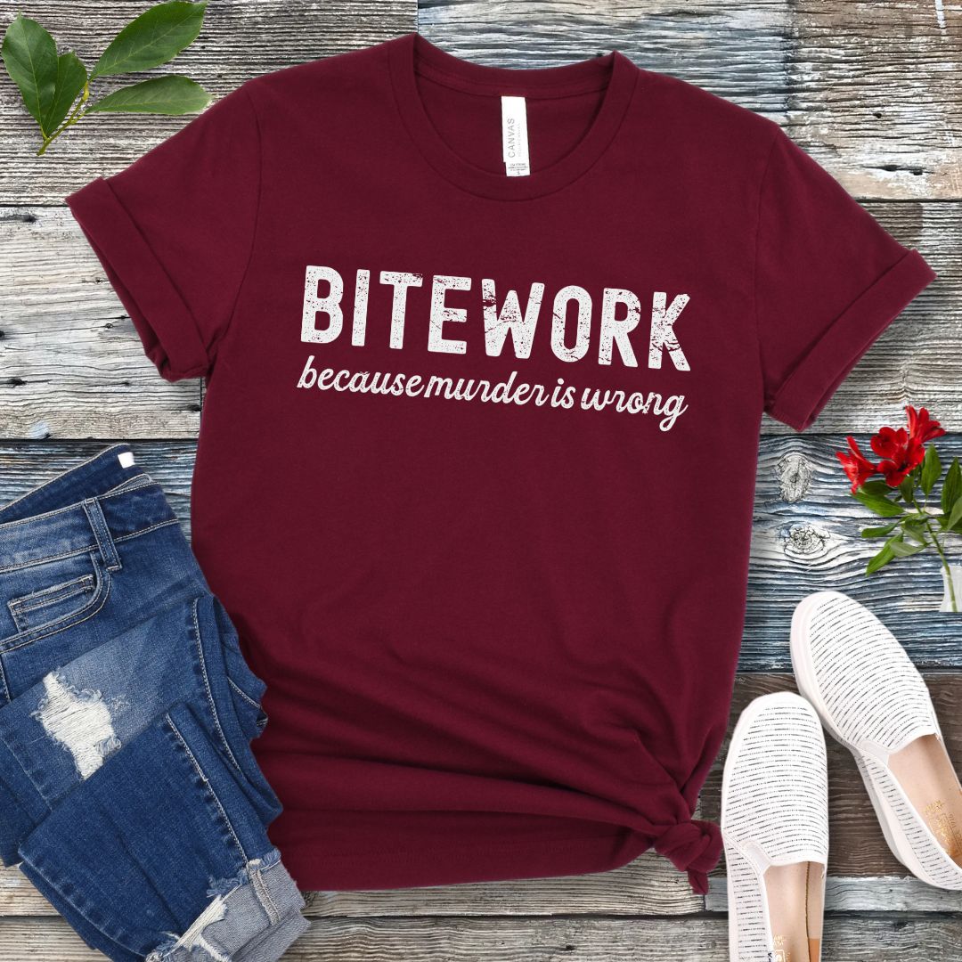 Maroon Schutzhund t-shirt with 'BITEWORK because murder is wrong' text on a wooden surface with jeans and shoes.