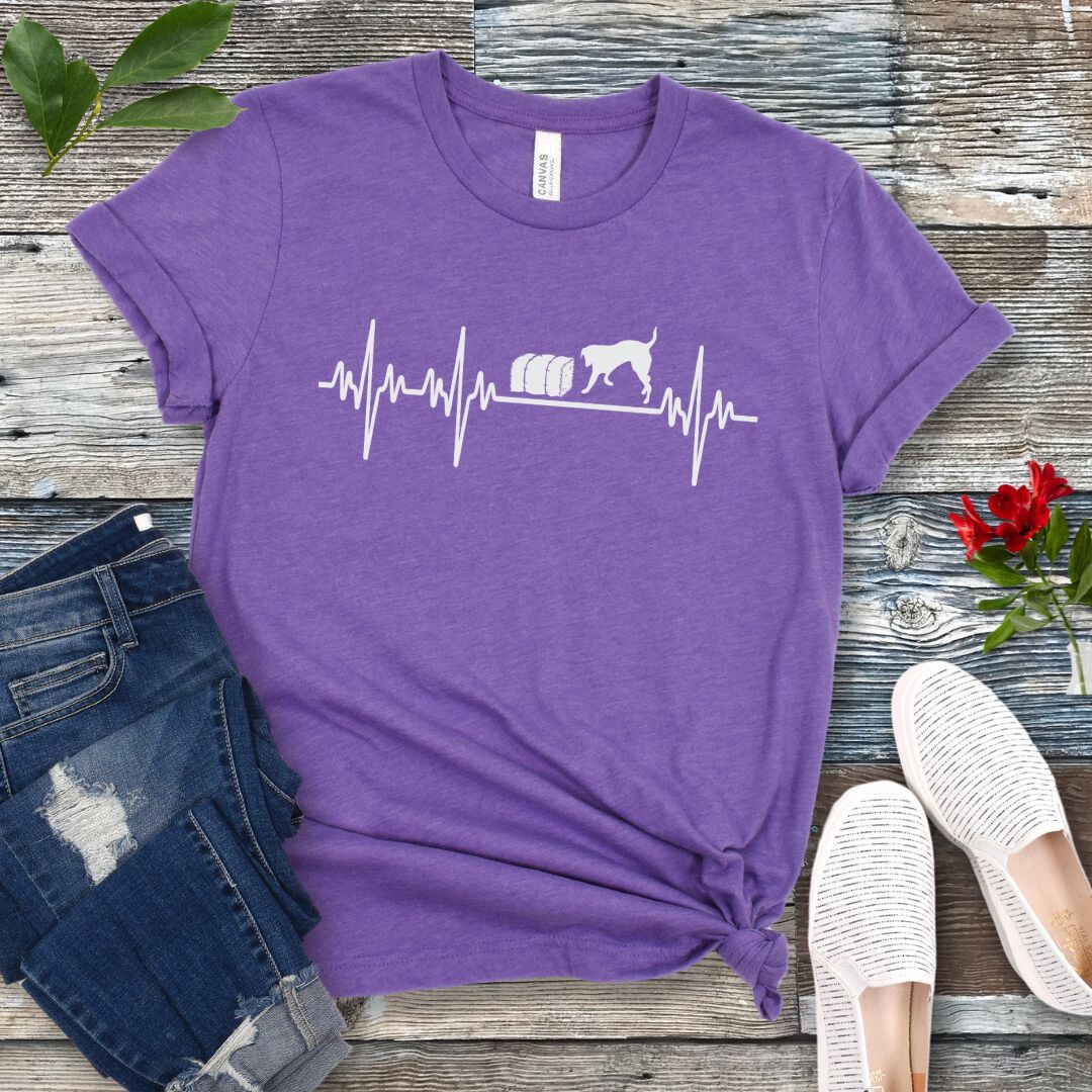 Purple dog sports t-shirt with heartbeat/EKG and barn hunt dog design on a wooden surface with jeans and shoes.