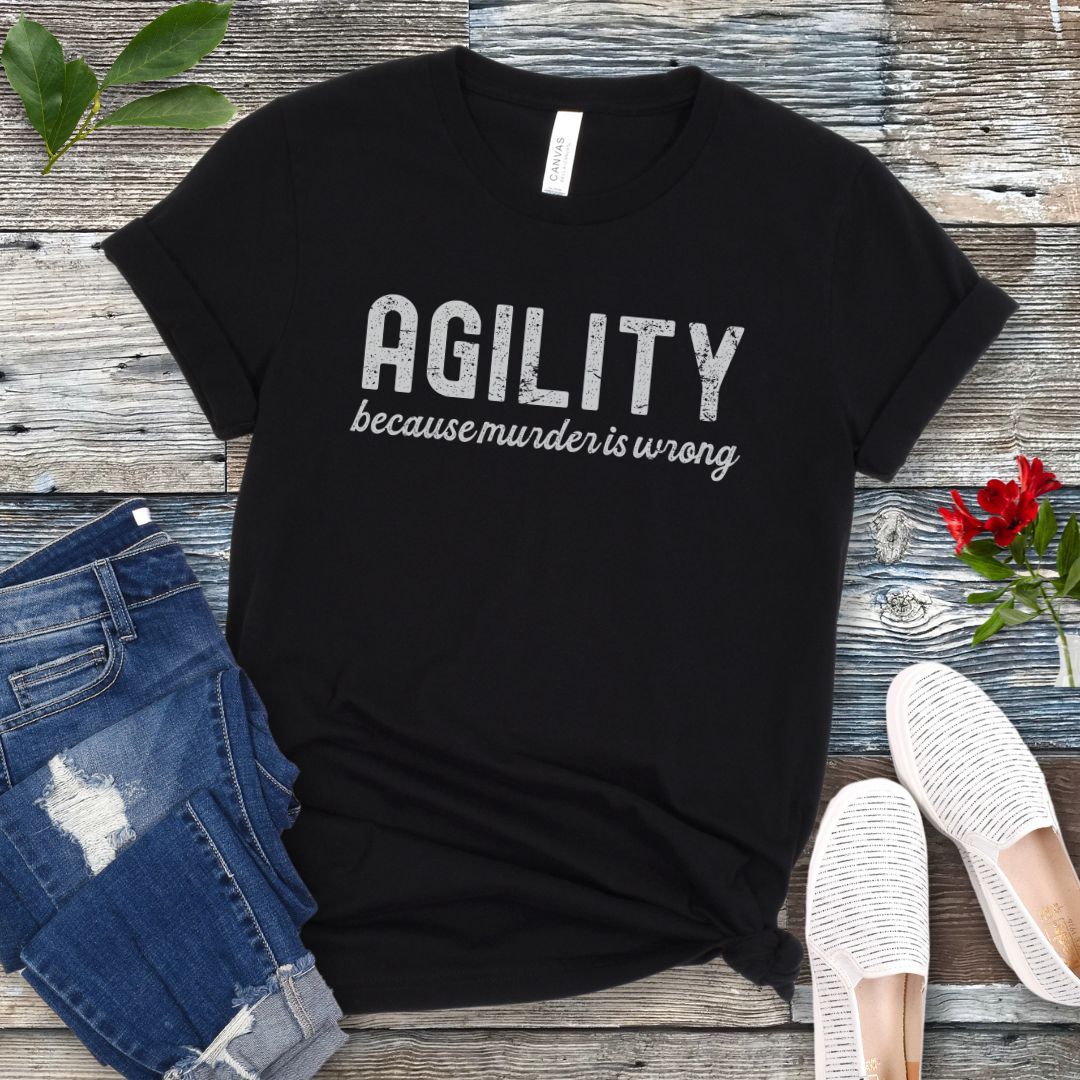 Black t-shirt with 'AGILITY because murder is wrong' text on a wooden surface with jeans and shoes.