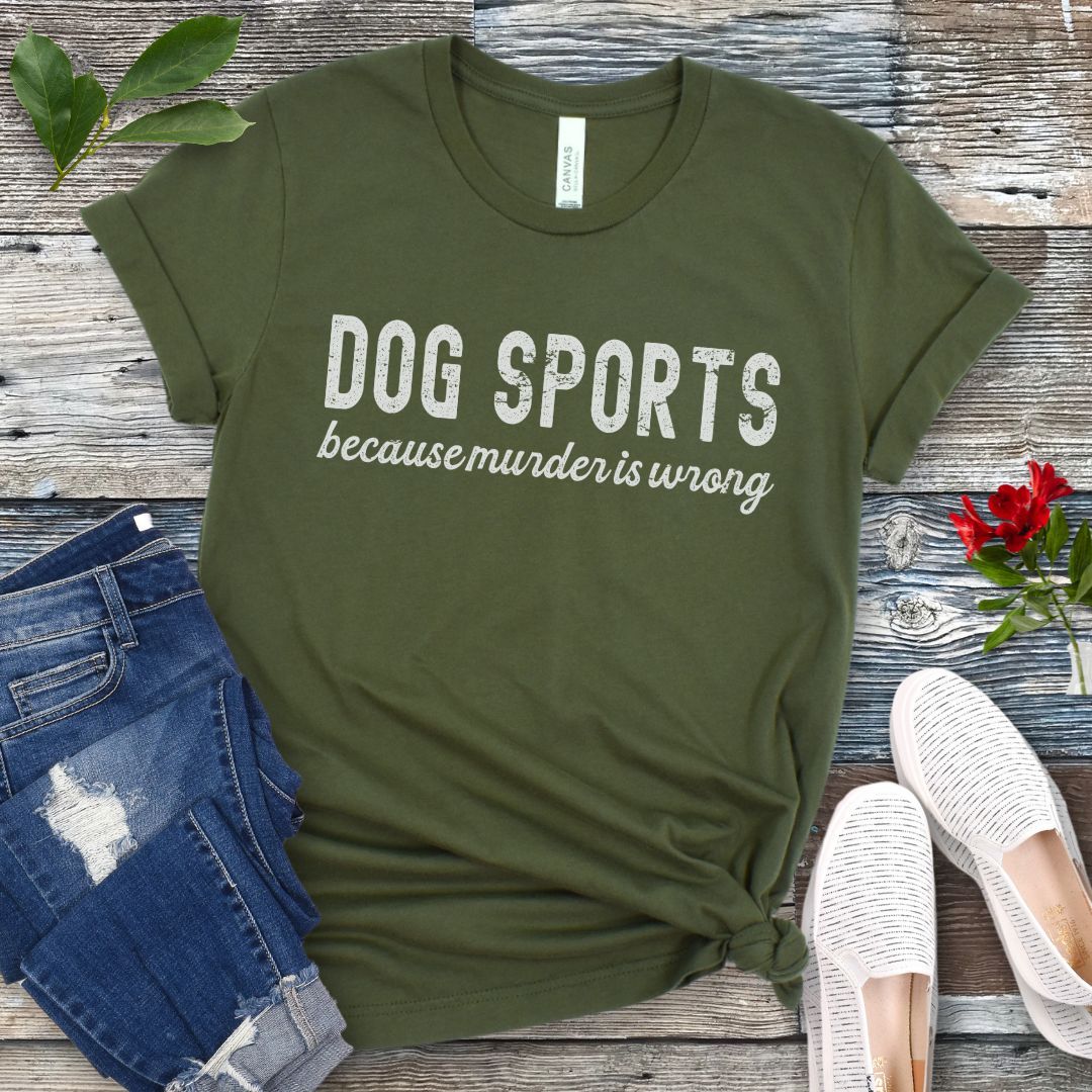 Green t-shirt with 'DOG SPORTS because murder is wrong' text on a wooden surface with jeans and shoes.