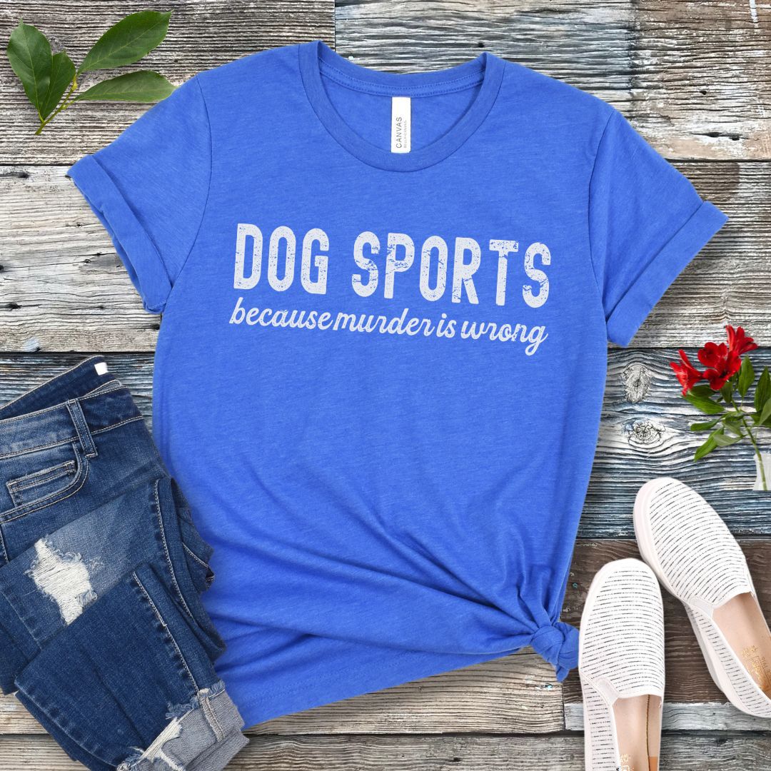 Blue t-shirt with 'DOG SPORTS because murder is wrong' text on a wooden surface with jeans and shoes.