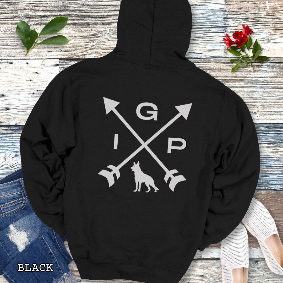 Black Schutzhund/IGP hoodie with crossed arrows design with 'IGP' text and German Shepherd silhouette on the back, presented on a wooden surface with accessories.