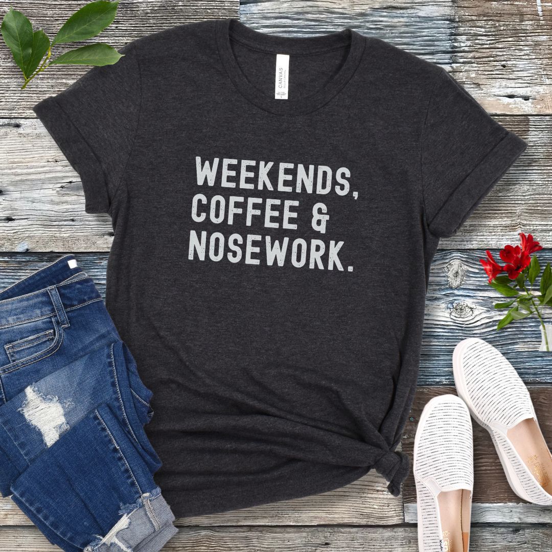 Dark grey green t-shirt with 'Weekends, Coffee & Nosework' text on a wooden surface with jeans and shoes.