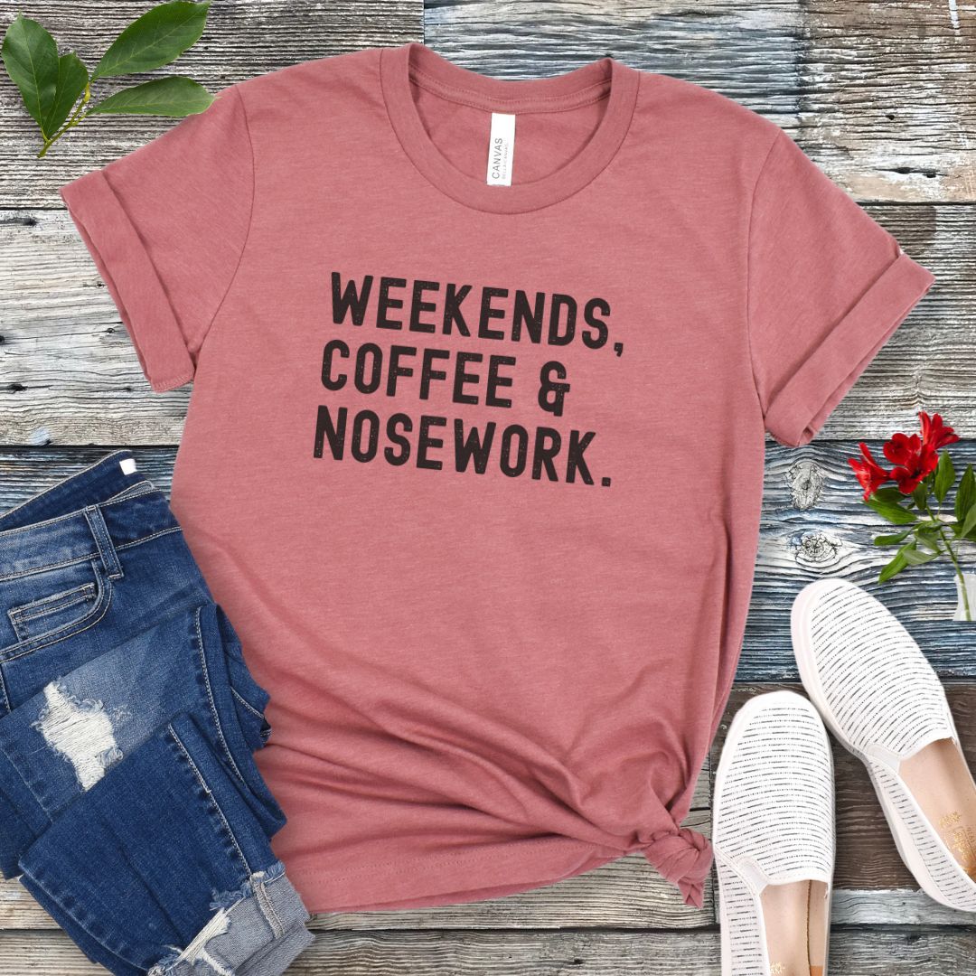 Mauve t-shirt with 'Weekends, Coffee & Nosework' text on a wooden surface with jeans and shoes.