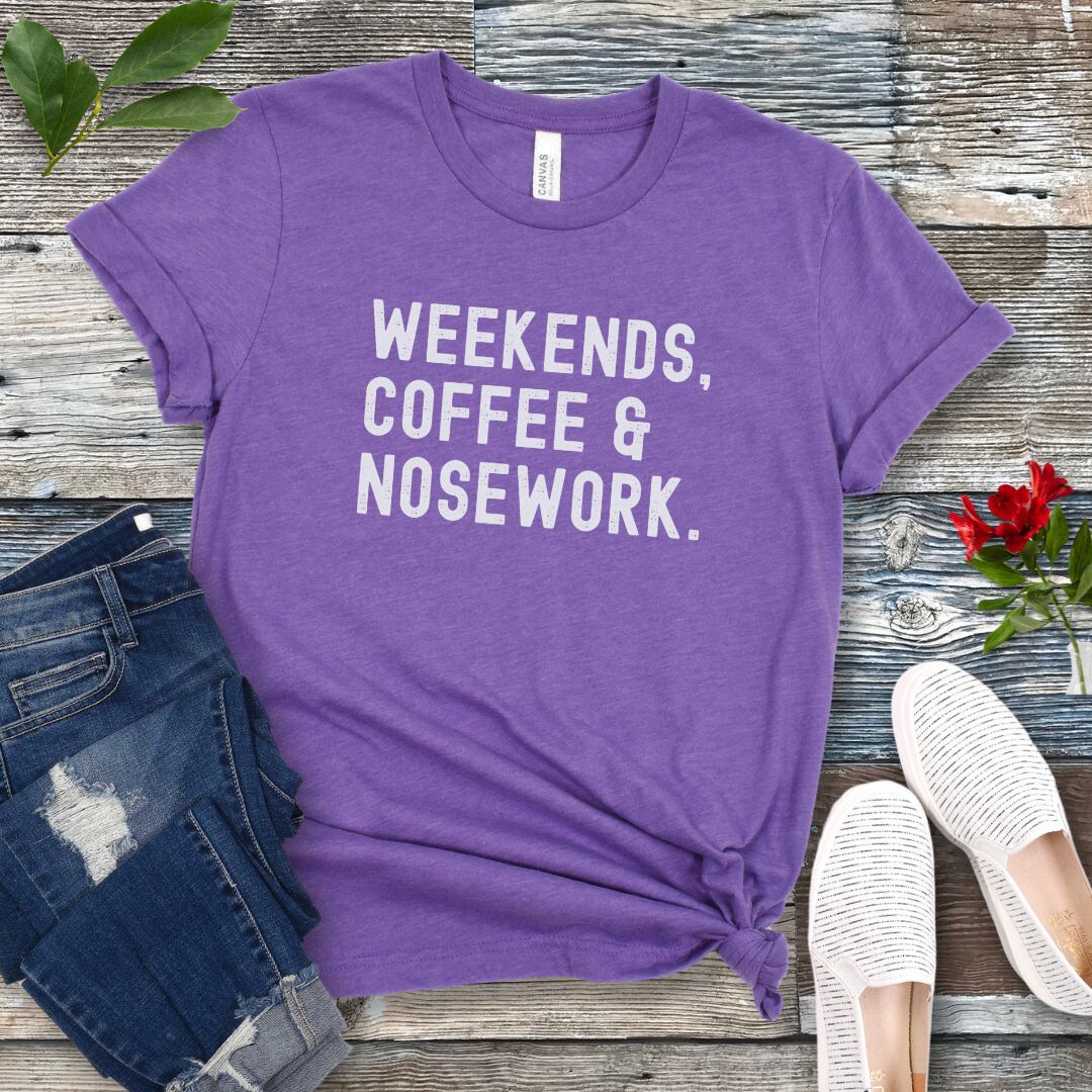 Purple dog sports t-shirt with 'Weekends, Coffee & Nosework' text on a wooden surface with jeans and shoes.