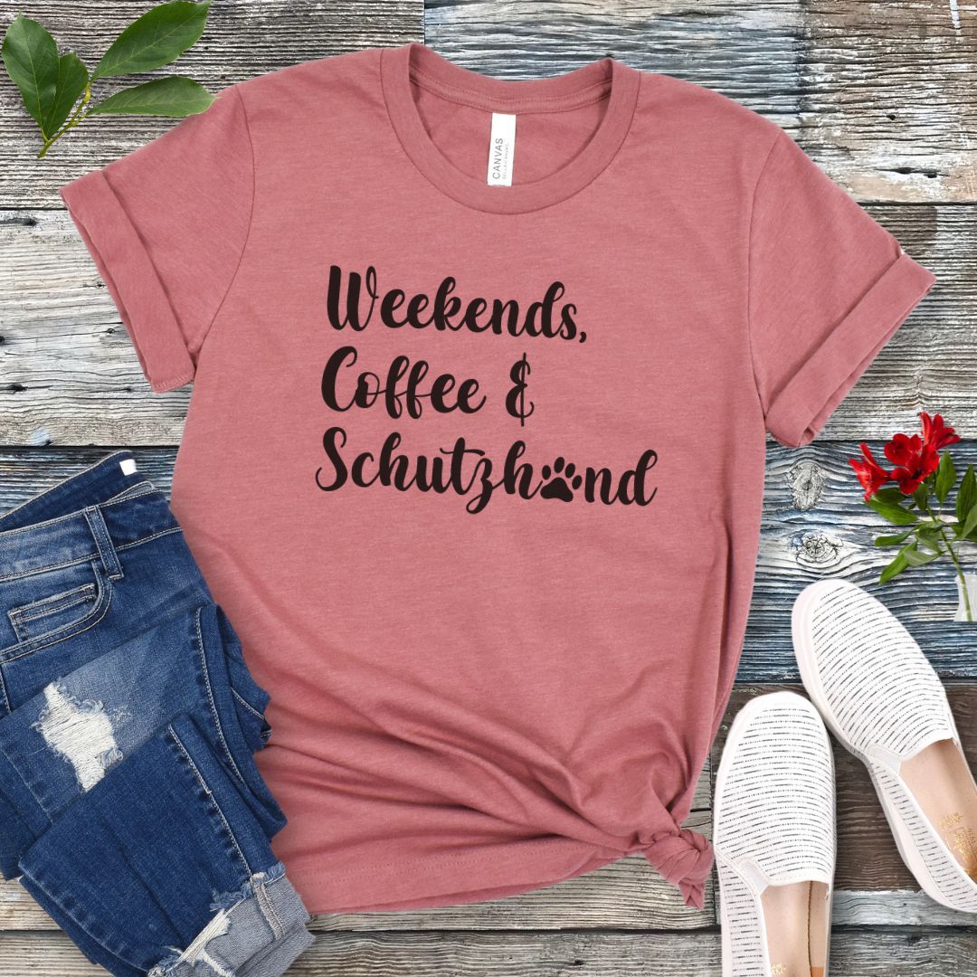 Mauve t-shirt with 'Weekends, Coffee & Schutzhund' text on a wooden surface with jeans and shoes.