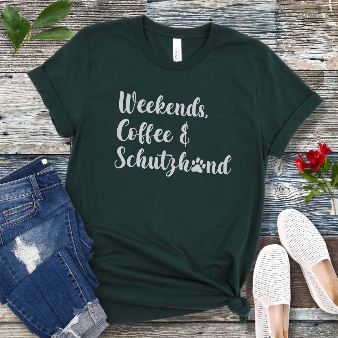 Dark green t-shirt with 'Weekends, Coffee & Schutzhund' text on a wooden surface with jeans and shoes.