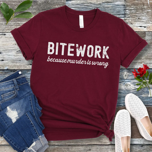 Maroon Schutzhund t-shirt with 'BITEWORK because murder is wrong' text on a wooden surface with jeans and shoes.