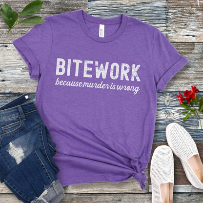 Purple Schutzhund t-shirt with 'BITEWORK because murder is wrong' text on a wooden surface with jeans and shoes.