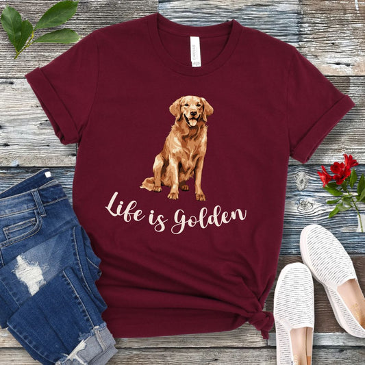 Maroon t-shirt with a Golden Retriever illustration and 'Life is Golden' text on a wooden surface with jeans and shoes.