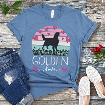 Blue t-shirt with a graphic of a Golden Retriever surrounded by hearts and a vintage sunset, and 'Golden Love' text below, presented on a wooden surface with jeans and shoes.