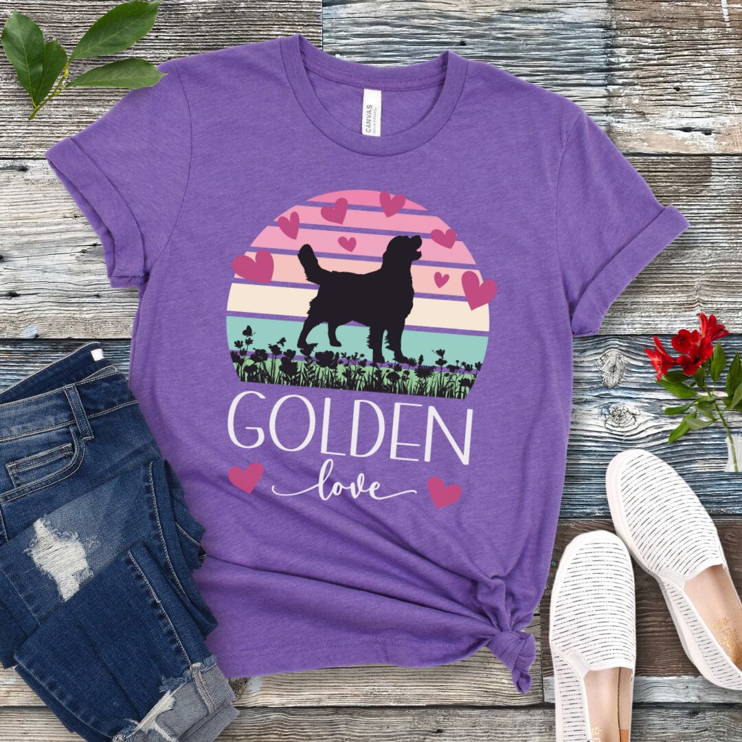 Purple dog mom t-shirt with a graphic of a Golden Retriever surrounded by hearts and a vintage sunset, and 'Golden Love' text below, presented on a wooden surface with jeans and shoes.