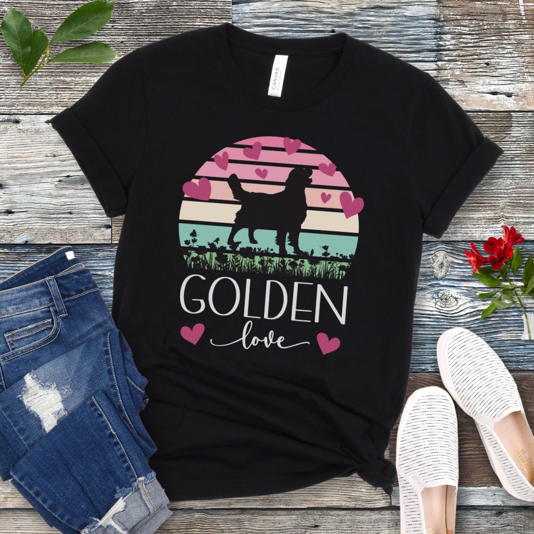 Black dog lover t-shirt with a graphic of a Golden Retriever surrounded by hearts and a vintage sunset, and 'Golden Love' text below, presented on a wooden surface with jeans and shoes.