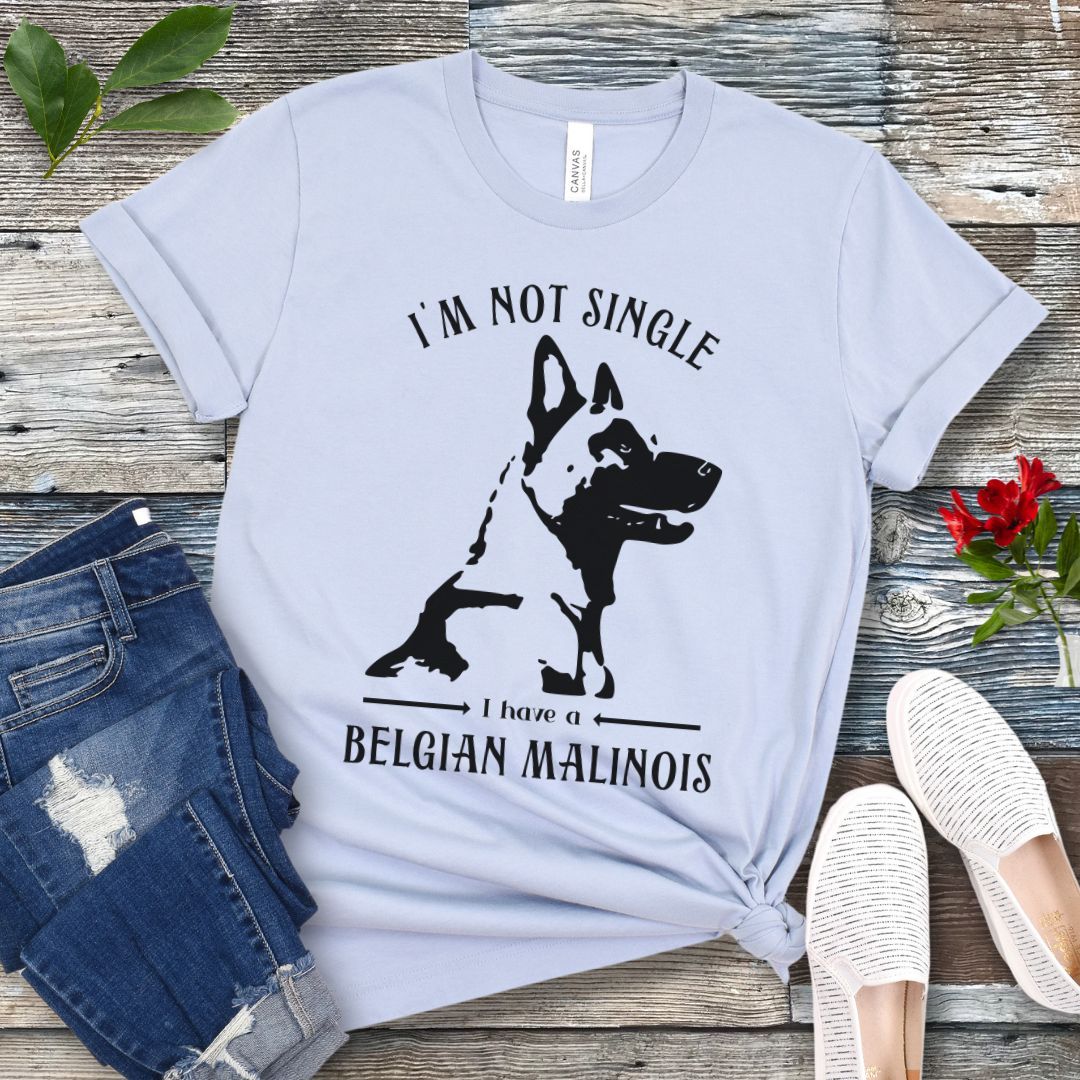 Light blue t-shirt with "I'm Not Single I have a Belgian Malinois" text and silhouette of a Belgian Malinois dog printed on it, displayed flat with a pair of jeans and white shoes on a wooden surface.