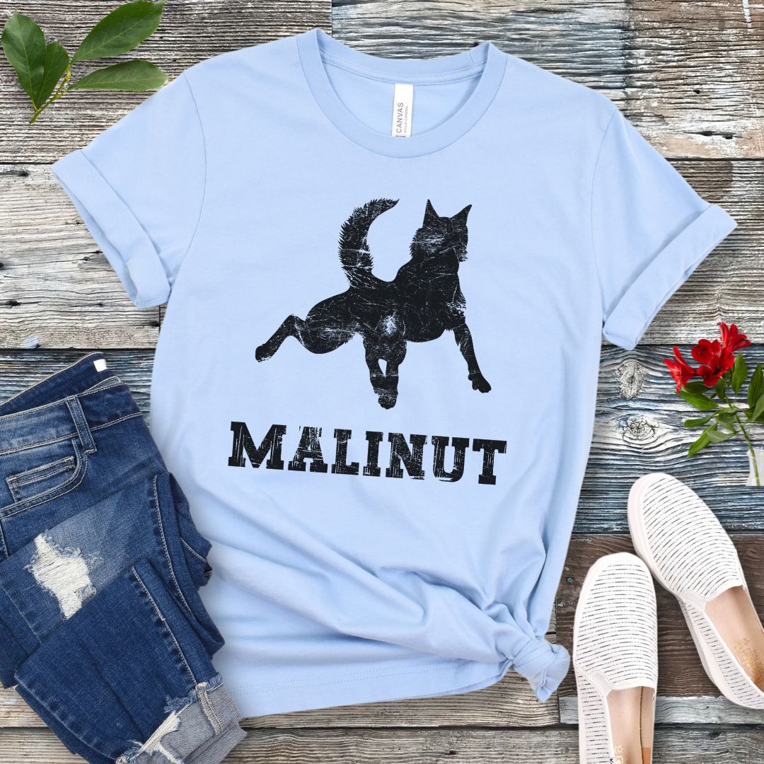 Light blue t-shirt with leaping Belgian Malinois silhouette and 'MALINUT' text on a wooden surface with jeans and shoes.
