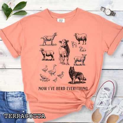 Orange Comfort Colors t-shirt for Belgian Tervuren lovers with vintage farm animal illustrations and a Belgian Tervuren dog, with the humorous text 'Now I've Herd Everything', shown on a wooden surface with denim jeans and flowers.