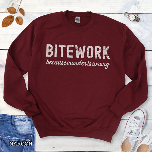 Maroon Schutzhund sweatshirt with 'BITEWORK because murder is wrong' text on a wooden surface with jeans and shoes.