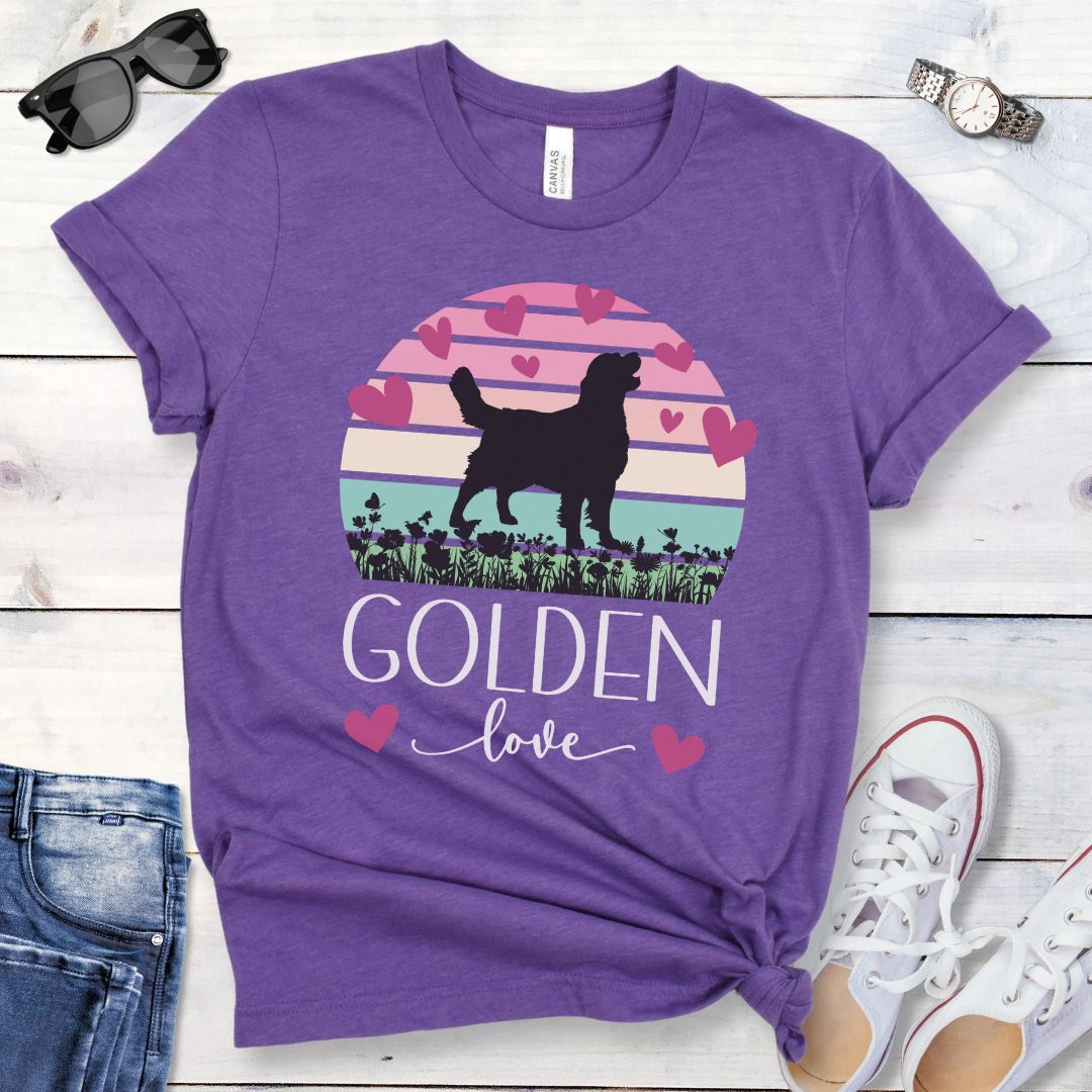 Purple dog lover t-shirt with a graphic of a Golden Retriever surrounded by hearts and a pastel vintage sunset, and 'Golden Love' text below, presented on a wooden surface with jeans and shoes.
