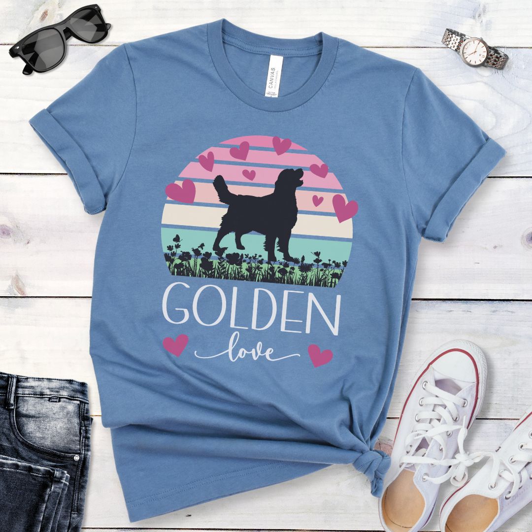 Blue t-shirt with a graphic of a Golden Retriever surrounded by hearts and a pastel vintage sunset, and 'Golden Love' text below, presented on a wooden surface with jeans and shoes.