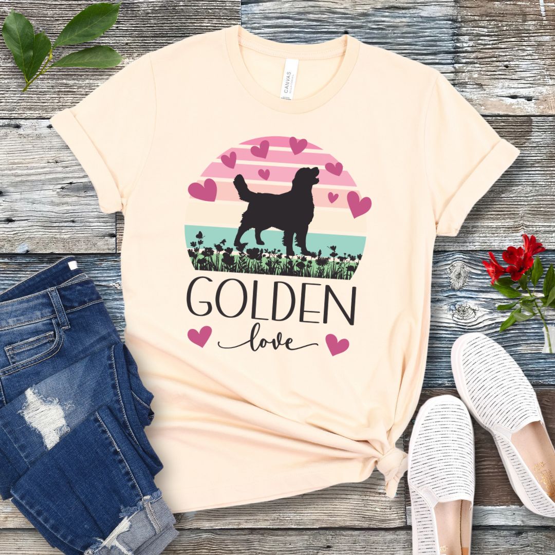 Beige t-shirt with a graphic of a Golden Retriever surrounded by hearts and a pastel vintage sunset, and 'Golden Love' text below, presented on a wooden surface with jeans and shoes.