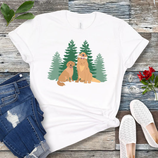 White dog lover t-shirt with graphic of 2 Golden Retrievers in front of an evergreen forest, shown on a wooden surface with jeans and shoes.