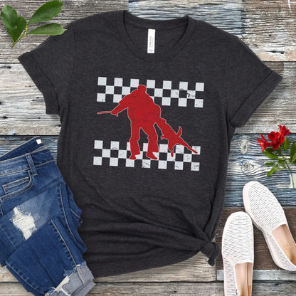 Dark grey bitework t-shirt with protection dog, K9 helper, and checkerboard design, presented on a wooden surface with jeans and shoes.