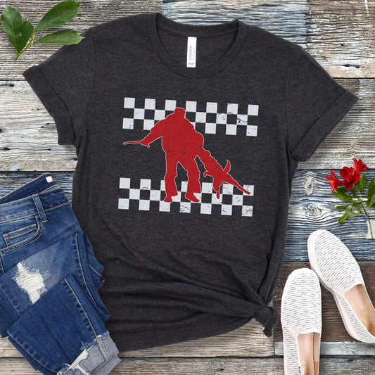 Dark grey bitework t-shirt with protection dog, K9 helper, and checkerboard design, presented on a wooden surface with jeans and shoes.