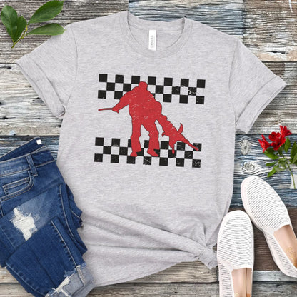 Light grey bite work t-shirt with protection dog, K9 helper, and checkerboard design, presented on a wooden surface with jeans and shoes.
