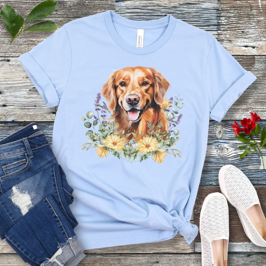 Light blue dog lover t-shirt with a watercolor design of a Golden Retriever dog surrounded by colorful wildflowers, shown on a wooden surface with jeans and shoes.