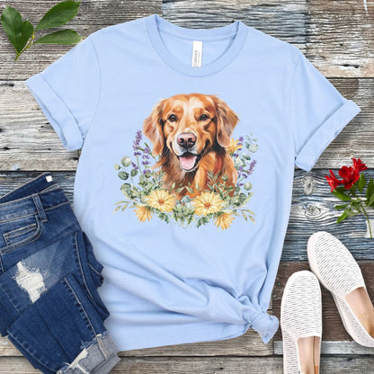 Light blue dog lover t-shirt with a watercolor design of a Golden Retriever dog surrounded by colorful wildflowers, shown on a wooden surface with jeans and shoes.