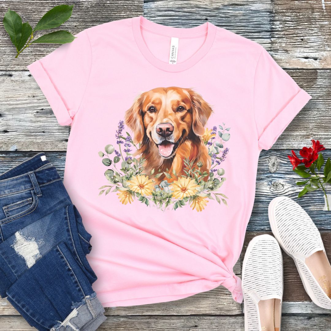 Pink dog lover t-shirt with a watercolor design of a Golden Retriever dog surrounded by colorful wildflowers, shown on a wooden surface with jeans and shoes.