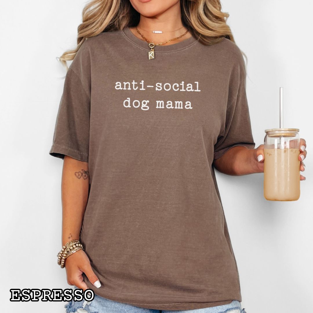 Person wearing a brown Comfort Colors dog lover t-shirt with 'anti-social dog mama' text, holding a drink against a white background