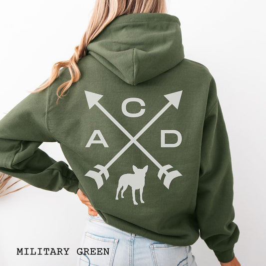 Military green Cattle Dog hoodie with back print design of crossed arrows, 'ACD' text and an Australian Heeler silhouette, worn by a person, on a white background.
