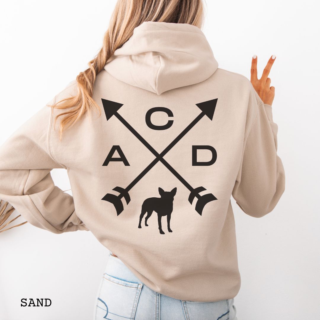 Beige Cattle Dog hoodie with back print design of crossed arrows, 'ACD' text and an Australian Heeler silhouette, worn by a person, on a white background.