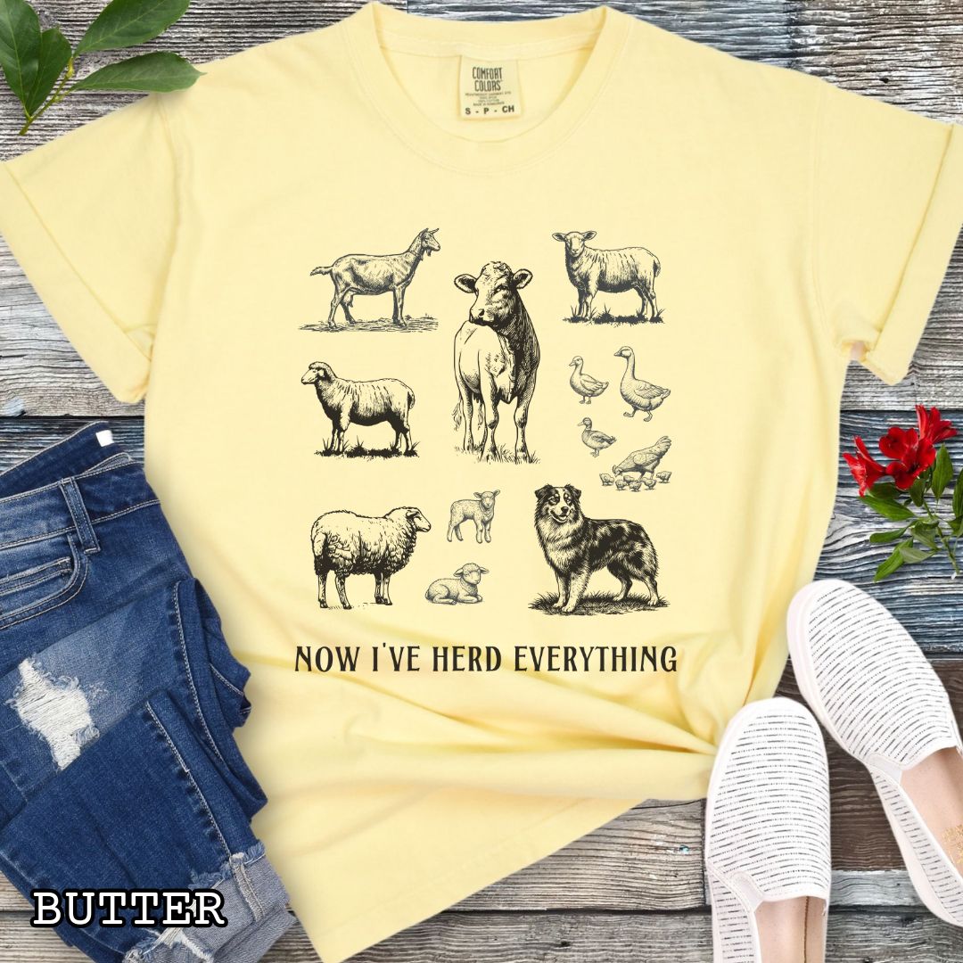 Yellow Comfort Colors t-shirt for Australian Shepherd lovers with vintage farm animal illustrations and an Australian Shepherd dog, with the humorous text 'Now I've Herd Everything', shown on a wooden surface with denim jeans and flowers.