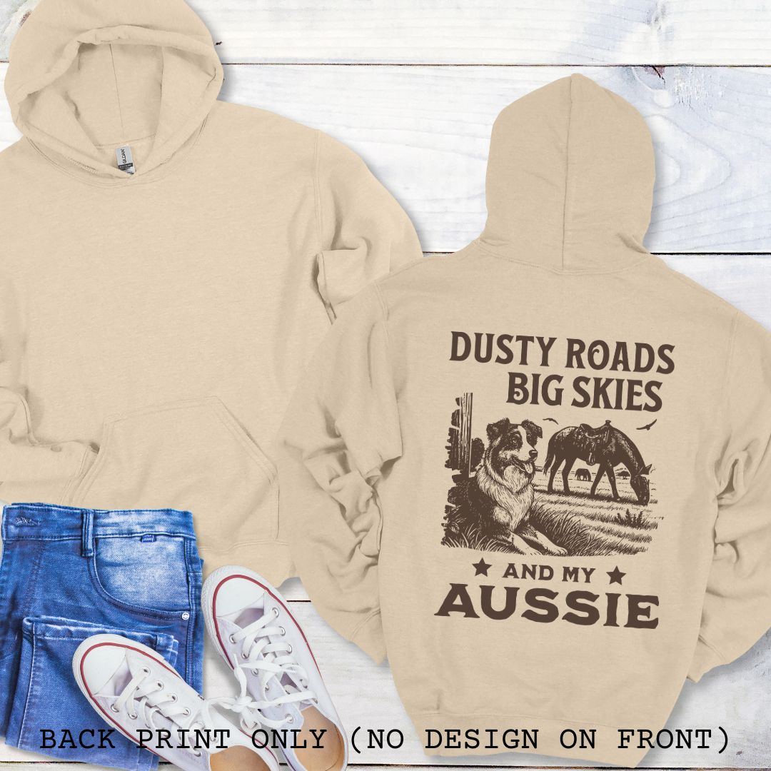 Beige hoodie with 'Dusty Roads Big Skies and My Aussie' text and graphic, paired with jeans and sneakers on a light wooden surface.