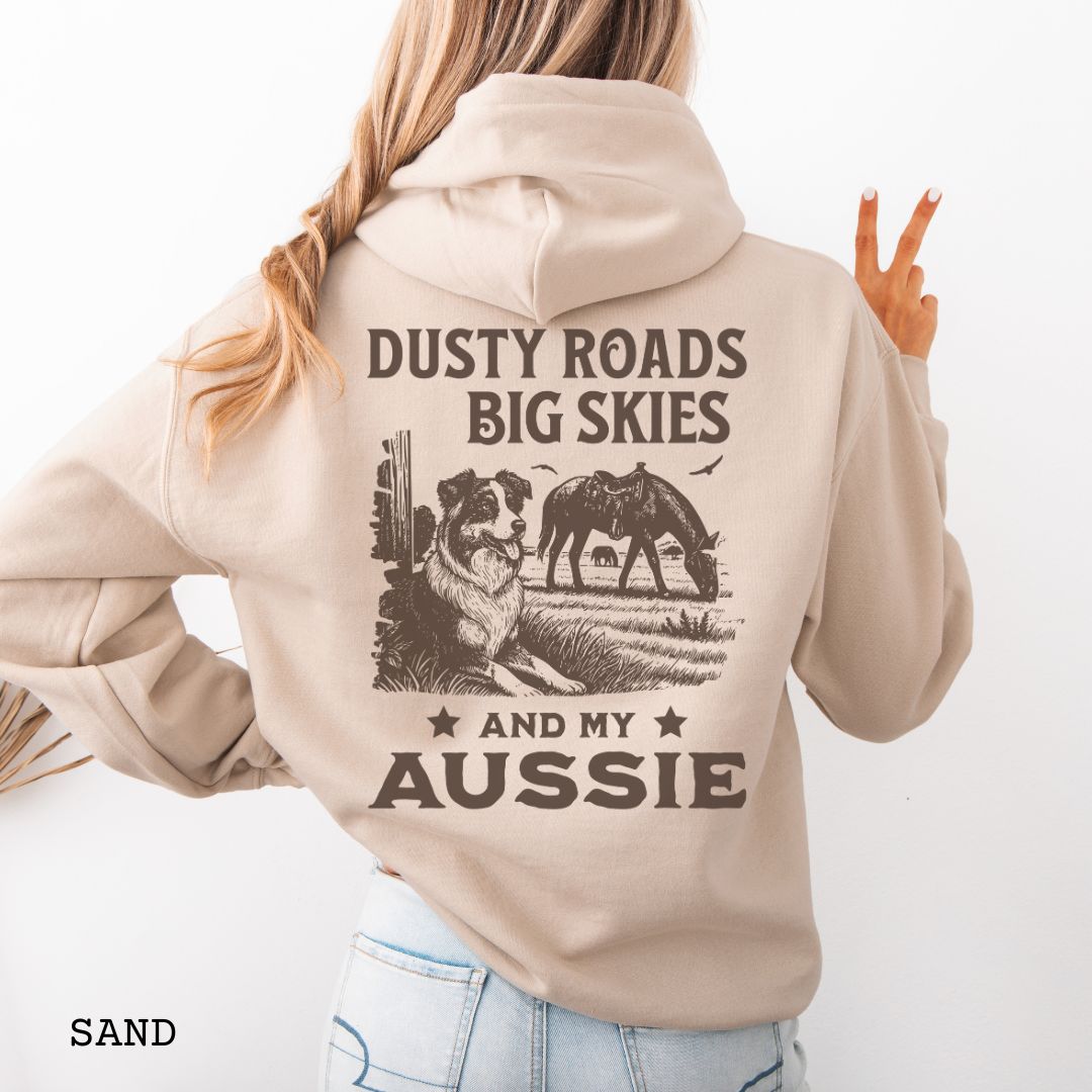 Back view of sand-beige Australian Shepherd hoodie featuring a Western-style design with grazing horse, rustic fence, and an Australian Shepherd illustration; text reads “Dusty Roads, Big Skies, and My Aussie.”