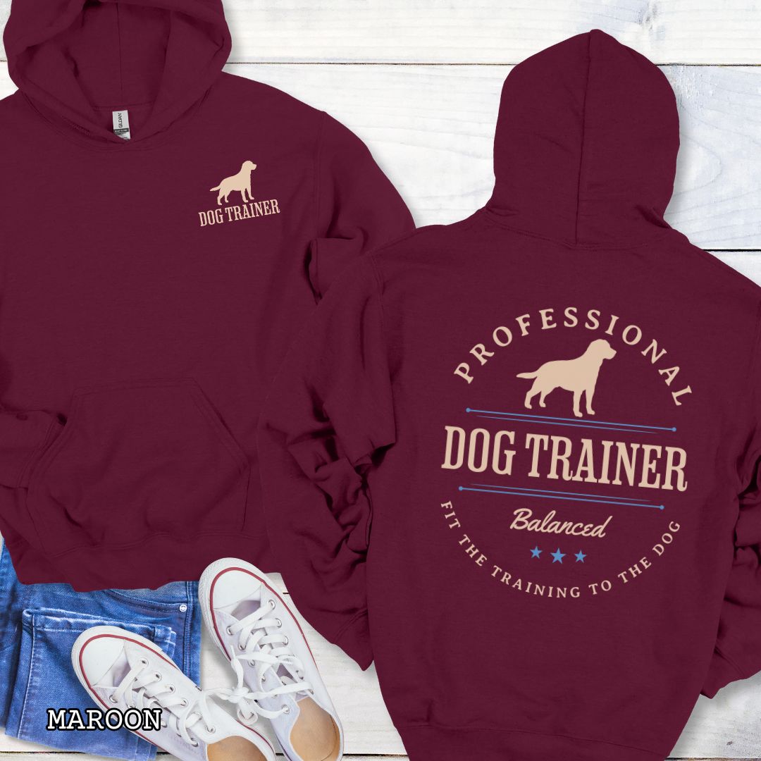 Front and back view of a maroon dog training hoodie with the text 'PROFESSIONAL DOG TRAINER, Balanced, Fit the Training to the Dog"' and custom dog breed silhouette in a vintage, badge style design. The shirt is displayed flat with a pair of blue jeans and white shoes.