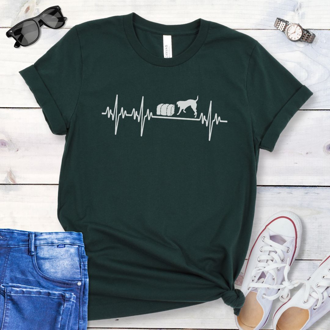 Dark green dog sports t-shirt with heartbeat/EKG and barn hunt dog design on a wooden surface with jeans and shoes.