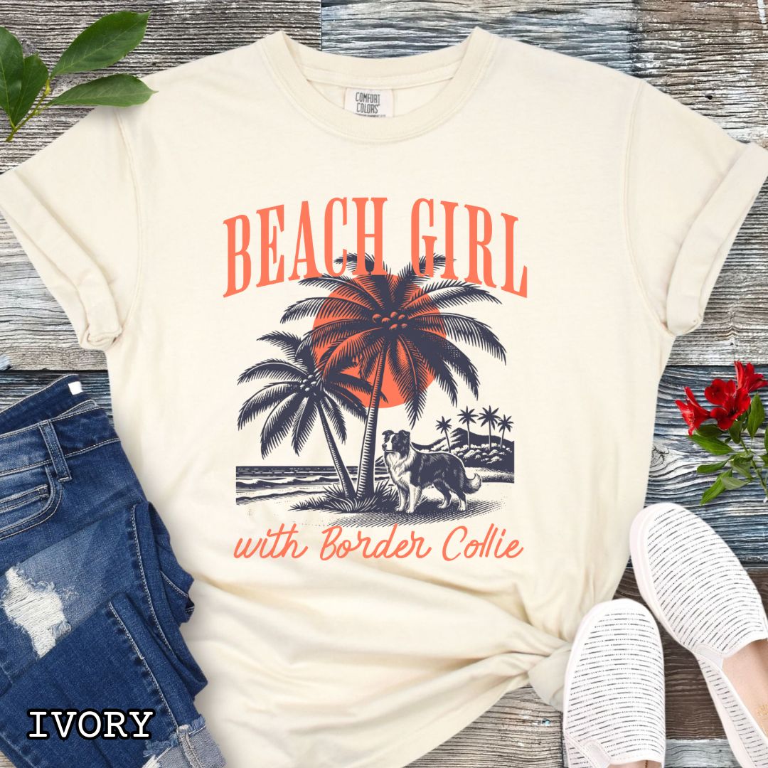 Beige Comfort Colors t-shirt for Border Collie lovers with graphic of a Border Collie standing on a tropical beach, and the text 'Beach Girl With Border Collie' in retro lettering, shown on a wooden surface with accessories.