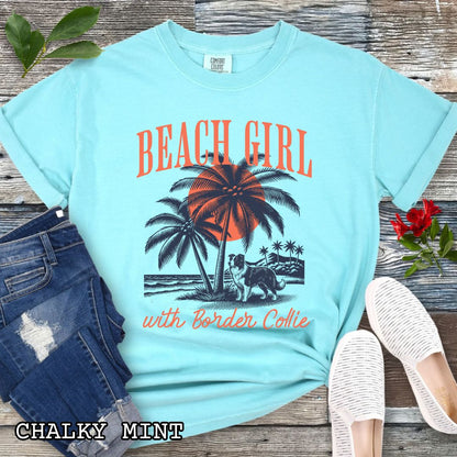 Mint Comfort Colors t-shirt for Border Collie lovers with graphic of a Border Collie standing on a tropical beach, and the text 'Beach Girl With Border Collie' in retro lettering, shown on a wooden surface with accessories.