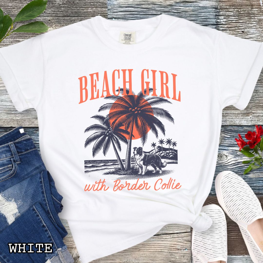 White Comfort Colors t-shirt for Border Collie lovers with graphic of a Border Collie standing on a tropical beach, and the text 'Beach Girl With Border Collie' in retro lettering, shown on a wooden surface with accessories.