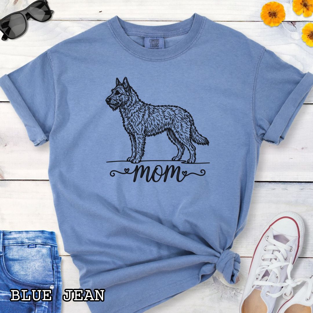 Blue Comfort Colors t-shirt with a vintage style illustration of a Belgian Laekenois and 'mom' text in feminine script beneath, shown on a wooden surface.