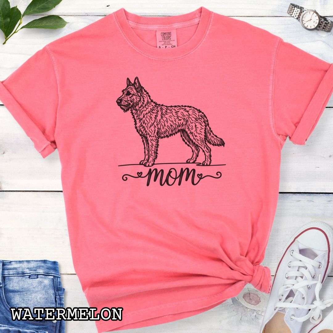 Pink Comfort Colors t-shirt with a vintage style illustration of a Belgian Laekenois and 'mom' text in feminine script beneath, shown on a wooden surface.