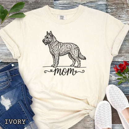 Beige Comfort Colors t-shirt with a vintage style illustration of a Belgian Laekenois and 'mom' text in feminine script beneath, shown on a wooden surface.