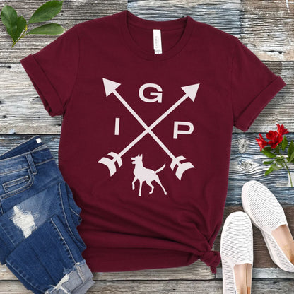 Maroon IGP dog  t-shirt with a graphic of crossed arrows, the letters IGP, and the silhouette of a Malinois, displayed on a wooden surface with a pair of jeans and white shoes in the background.