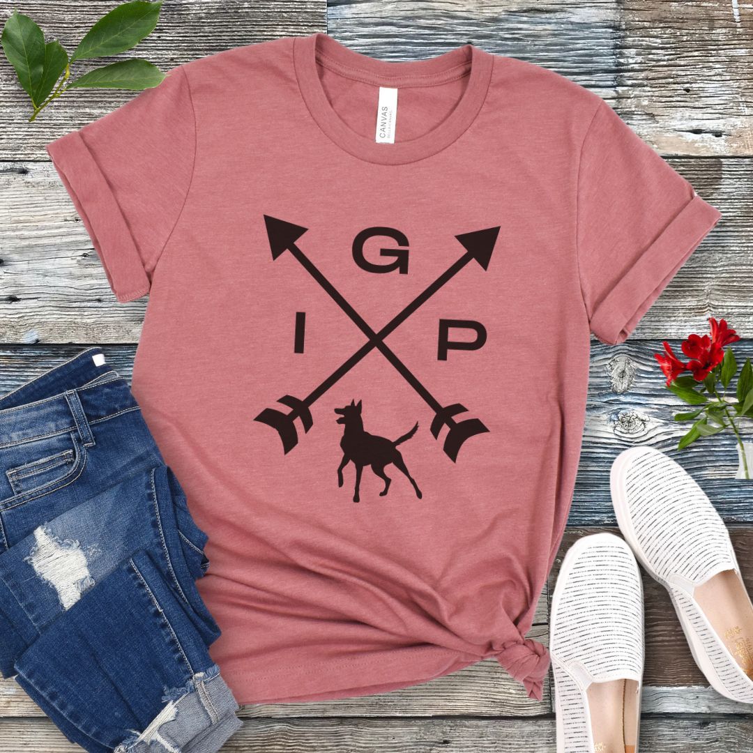 Mauve IGP dog  t-shirt with a graphic of crossed arrows, the letters IGP, and the silhouette of a Malinois, displayed on a wooden surface with a pair of jeans and white shoes in the background.