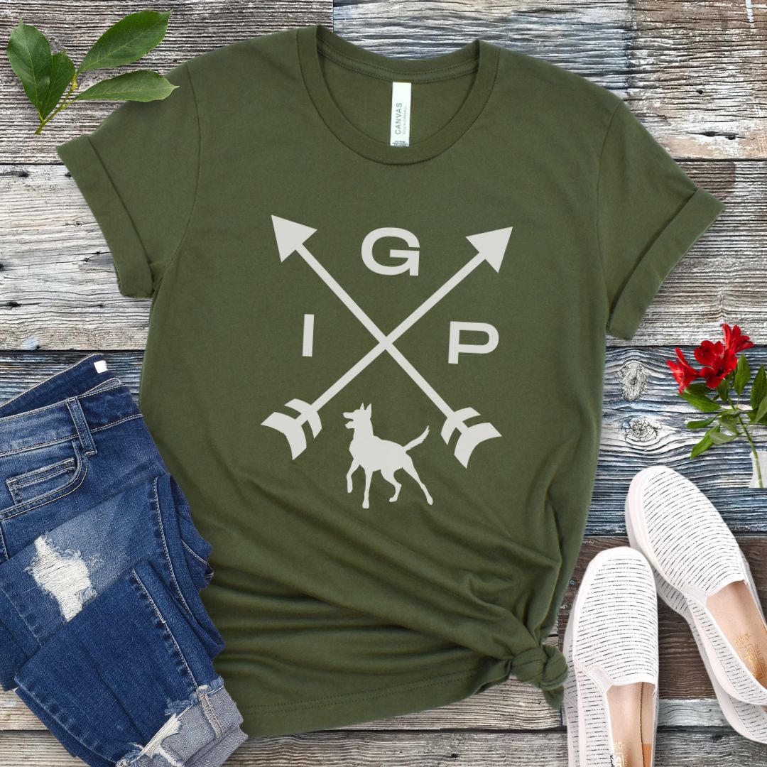 Military green IGP dog  t-shirt with a graphic of crossed arrows, the letters IGP, and the silhouette of a Malinois, displayed on a wooden surface with a pair of jeans and white shoes in the background.