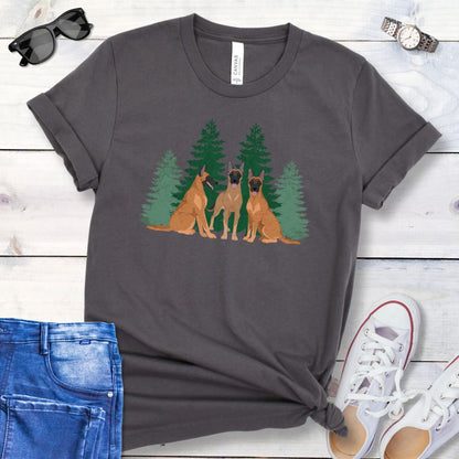 A dark grey unisex t-shirt with an image of 3 Belgian Malinois dogs and evergreen trees printed on it, displayed flat with a pair of jeans and white shoes on a wooden surface.